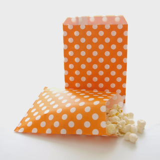 Orange polka dot popcorn bag with popcorn spilling out on a white background